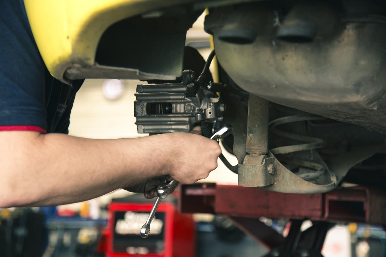 A mechanic working on a brake caliper with a car up on the ramp