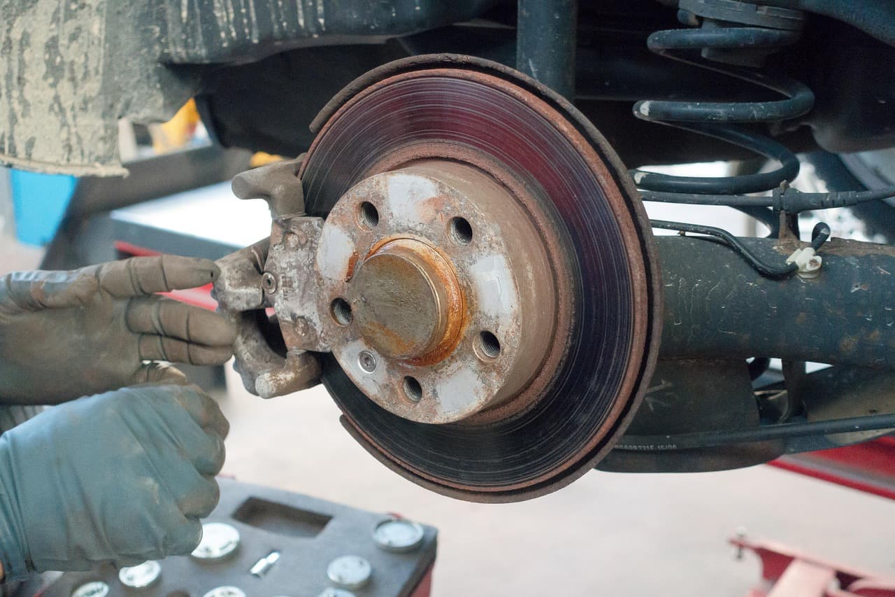 A brake disc and caliper being checked with gloved hands